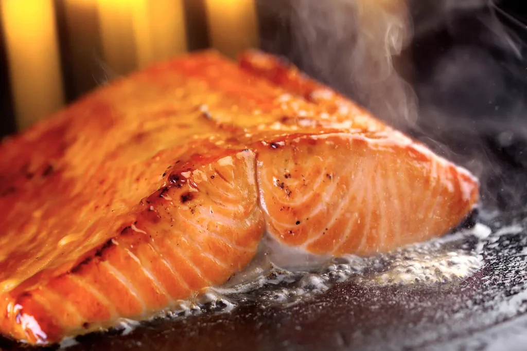 Salmon bubbling on cast iron surface with flames in the background and steam rising from surface photographed in Atlanta food photographer studio.